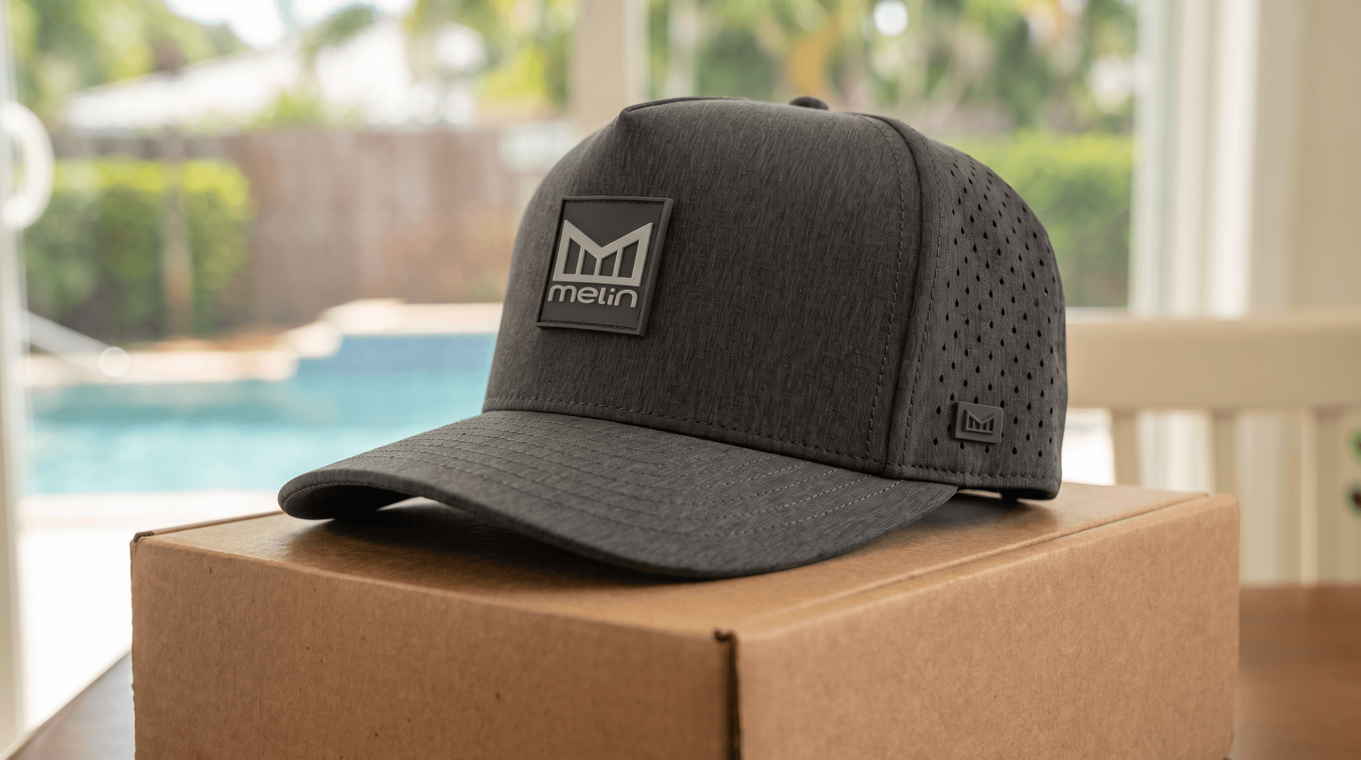 The Melin Odysea Stacked HYDRO in Heather Charcoal resting on its shipping box beside a backyard pool